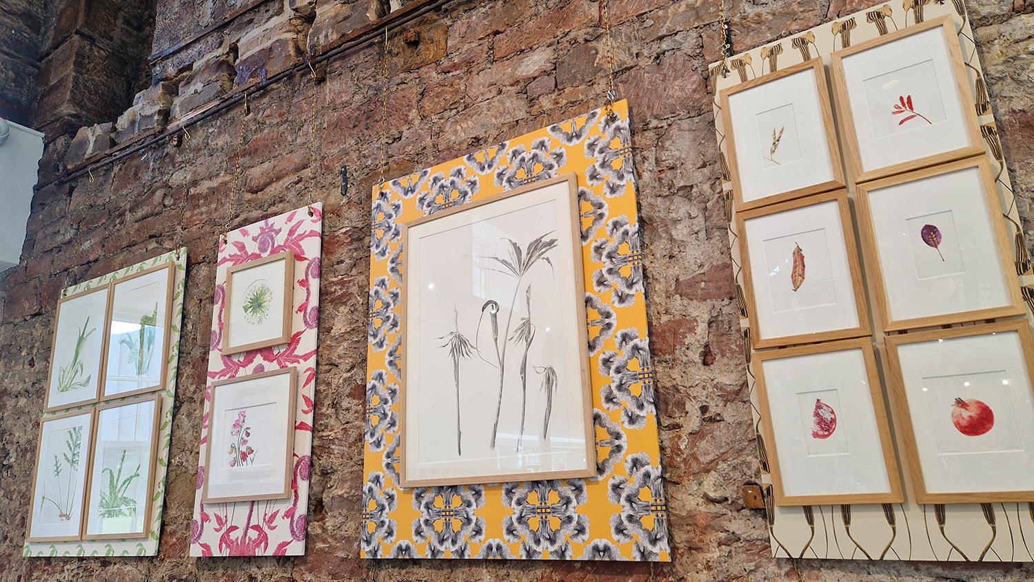 Artist Residency at Restoration Yard, Dalkeith Country Park, botanical art prints on wallpapered boards hanging on a stone and brick wall in the Foodhall