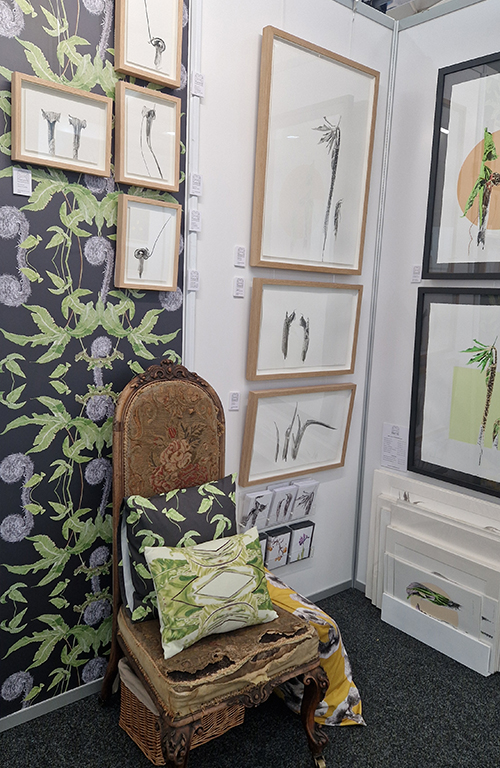 Marianne Hazlewood's Borders Art Fair display 2023, featuring botanical artwork, botanical wallpaper, cushions covered in botanical fabric, on an old chair